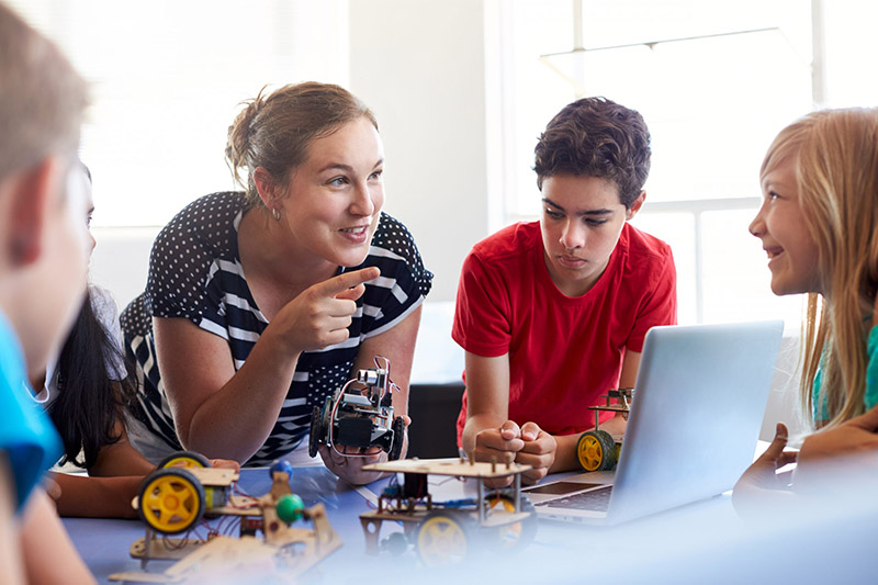 STEM teacher and students looking at a small robot in a classroom